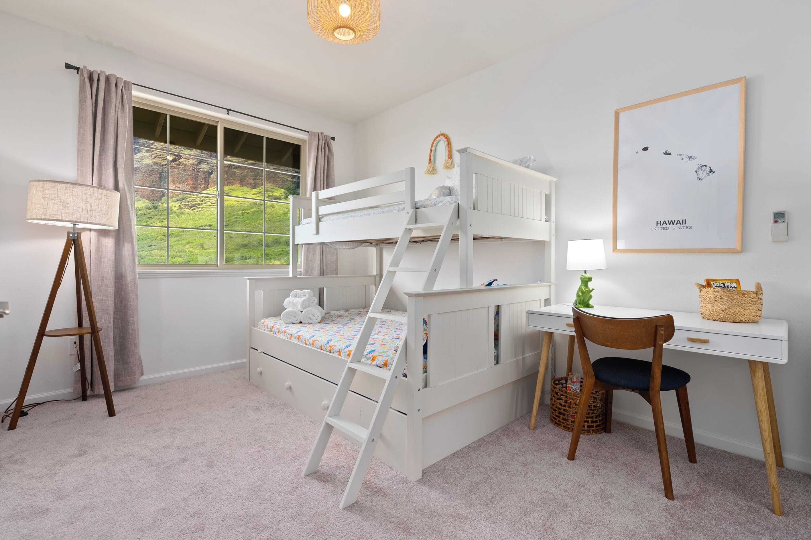 A bunk bed with a ladder, a desk with a chair, a lamp, and a framed map of Hawaii on the wall.