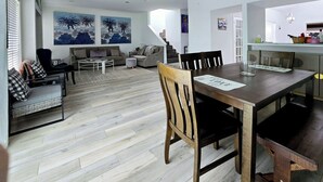 A modern living room with a dining area, featuring a wooden dining table, chairs, and a sofa.