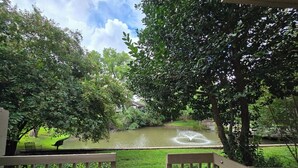 A view from a wooden deck overlooking a pond with a fountain, surrounded by lush greenery and trees.