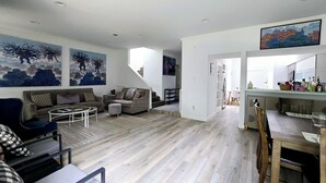 A spacious living area with a modern design, featuring a sofa set, a coffee table, and a dining table with chairs.