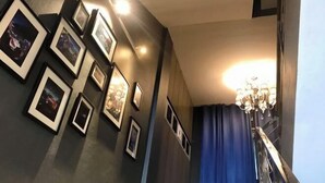 Un couloir orné de tableaux encadrés, un lustre et un rideau bleu.