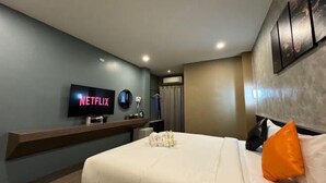 Une chambre d’hôtel moderne équipée d’un téléviseur à écran plat diffusant « NETFLIX », d’un lit avec des oreillers blancs et orange, d’une table de chevet et d’un climatiseur fixé au mur.