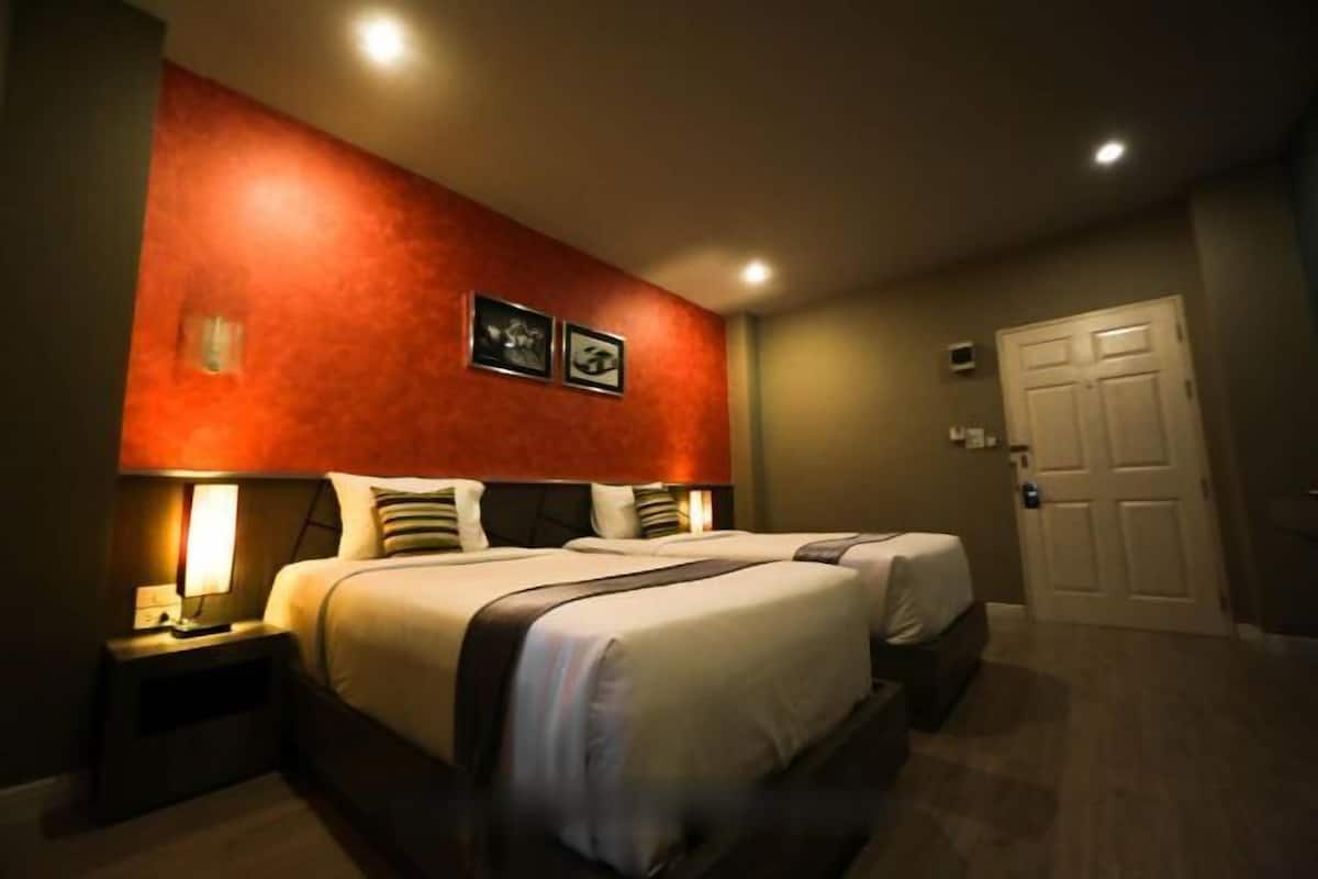 Una habitación de hotel con dos camas, una pared de acento roja y una puerta.