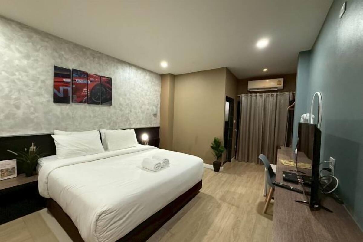 Una habitación de hotel con cama, escritorio con computadora, televisión y zona de ducha.