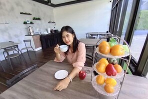 A person seated at a table with a tray of fruit and a bowl, in a room with a dining area and kitchen in the background. - The S Design Hotel (Buriram City)