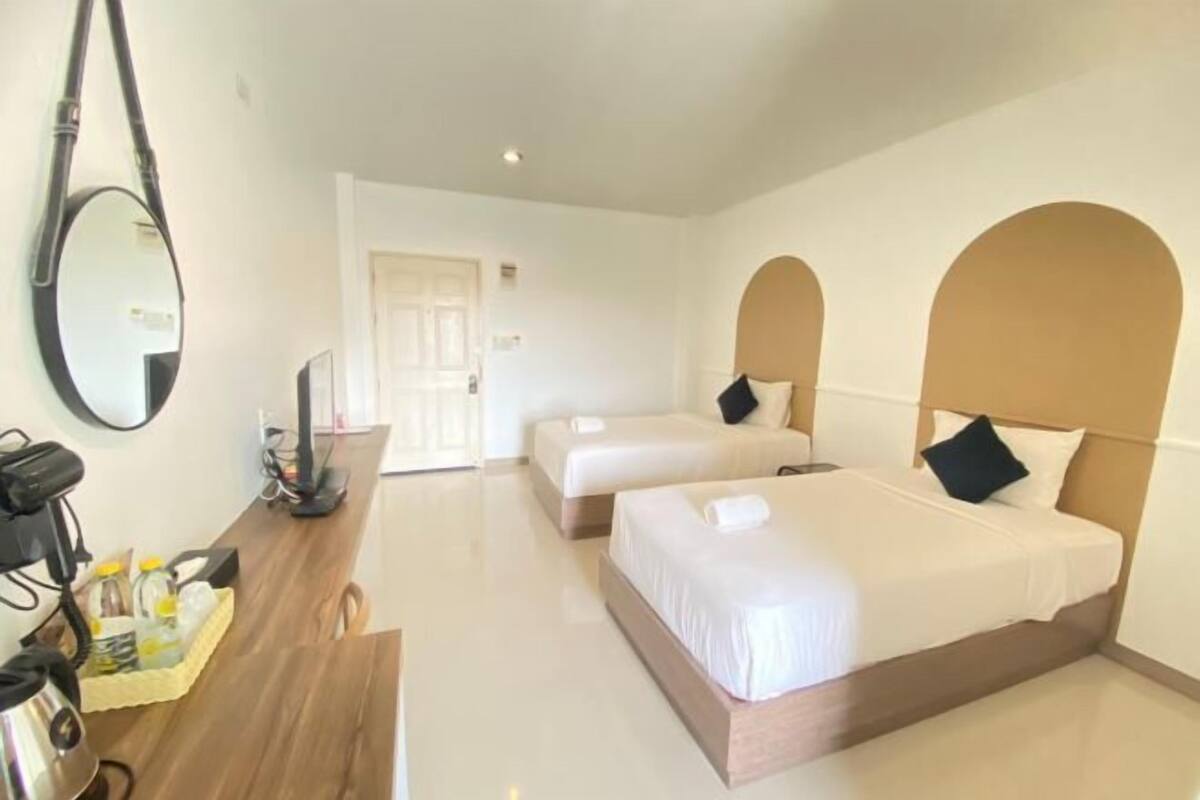 Habitación de hotel con dos camas, un escritorio con computadora, un espejo y una puerta que da a otra habitación.