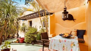 Eine Terrasse mit Tisch und Stühlen, umgeben von Topfpflanzen und einer Holzpergola.