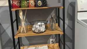 Une étagère de cuisine avec différentes tasses, une machine à café, un pot contenant des ustensiles et une serviette pliée.