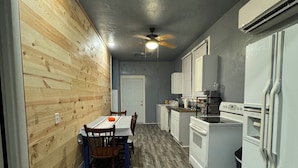 Une cuisine de taille réduite avec un revêtement mural en bois, un coin repas comprenant une table et des chaises, et des appareils électroménagers blancs.