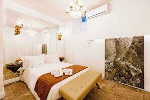 Ein Hotelzimmer mit einem Bett, einer Bank, einer Kandelaber und einem Gemälde an der Wand.