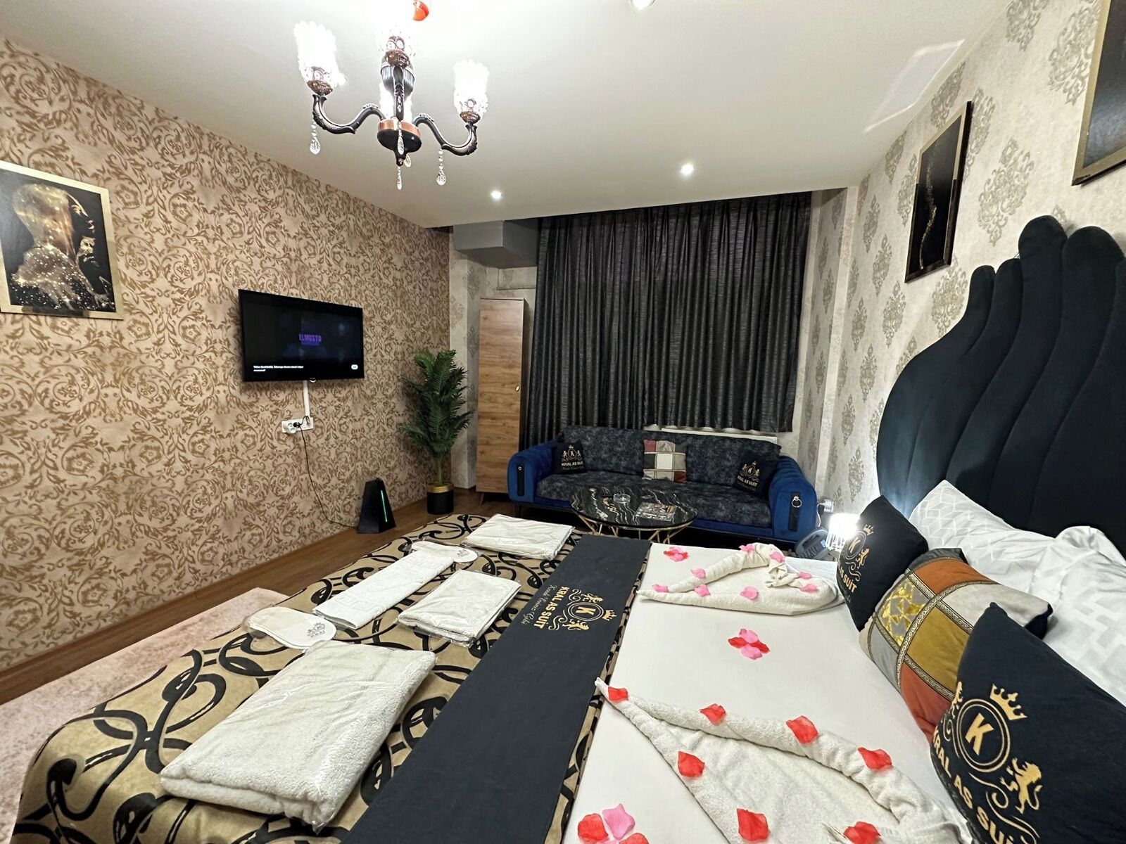 A hotel room with a large bed, a TV, a sofa, and a chandelier.