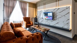 Ein modernes Hotelzimmer mit einer Couch, einem Sessel und einem Flachbildfernseher, der an einer Marmorwand angebracht ist.