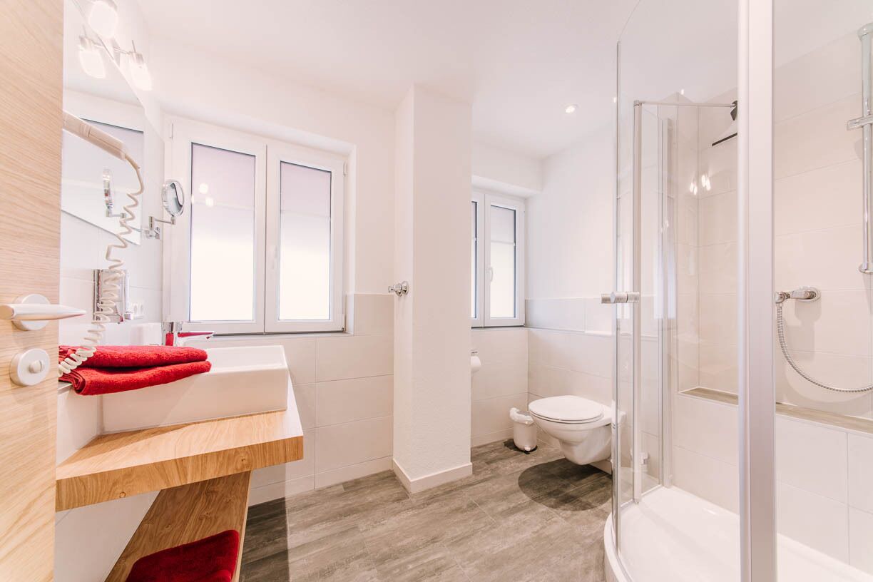 Ein modernes Badezimmer mit Duschkabine aus Glas, weißer Toilette und einem Holzwaschtisch mit Spiegel.