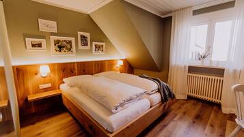 A bedroom with a wooden bed, a nightstand, a wall-mounted lamp, and framed pictures.