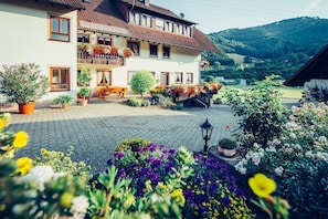 A two-story building with a balcony, potted plants, and a paved courtyard.