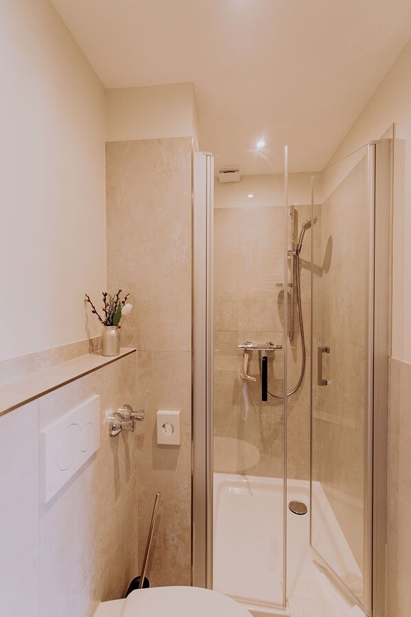 Un baño moderno con ducha envuelta en vidrio, un inodoro blanco y un pequeño estante con un florero.