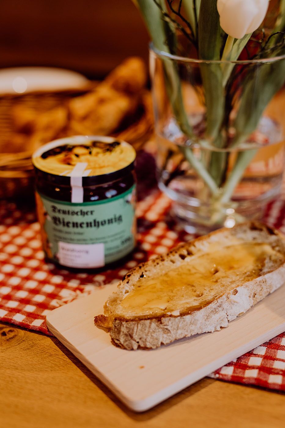 A slice of bread with butter on a white plate, a jar of Bratwurst Wienermagazine, and a glass with a white tulip.
