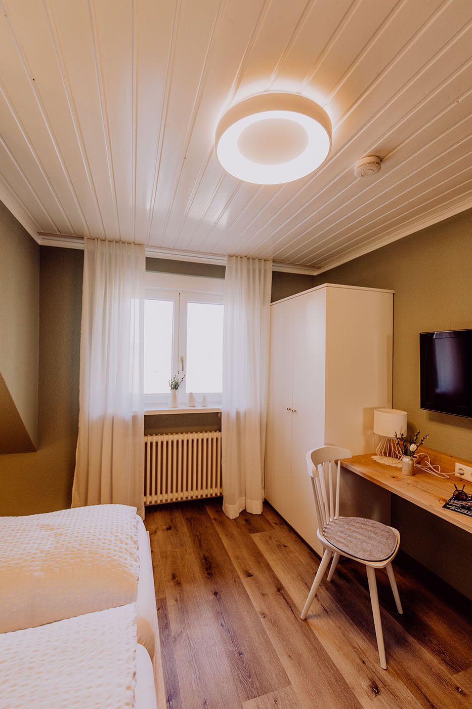 Ein Schlafzimmer mit einem Bett, einem Schreibtisch, einem Stuhl, einem Heizkörper und einem Fernseher.