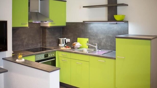 A kitchen with green cabinets, a stainless steel range hood, and a black countertop. - Schiebenrothenhof (Simonswald)
