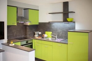 A kitchen with green cabinets, a stainless steel range hood, and a black countertop. - Schiebenrothenhof (Simonswald)