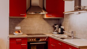 A kitchen with red cabinets, a stainless steel range hood, a coffee maker, and a sink. - Schiebenrothenhof (Simonswald)