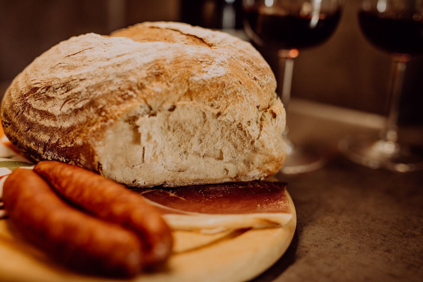 Una pagnotta con crosta dorata e mollica soffice, accompagnata da un salsiccia e una bottiglia di vino su un tavolo.