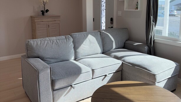 A modern living room with a grey sectional sofa, a wooden coffee table, and a white cabinet with decorative items.