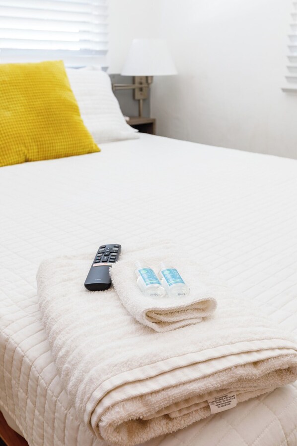 A neatly made bed with a white quilt, a folded towel, and a remote control. - Avila Suites (San Juan)