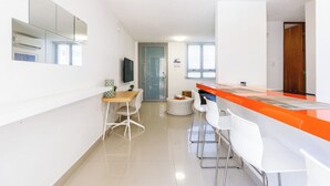 A modern kitchen with white cabinets, a wooden countertop, and a built-in oven. There are two white bar stools and a small round table. - Avila Suites (San Juan)