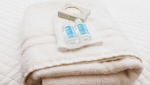 A neatly made bed with a folded white towel and two bottles of hand sanitizer. - Avila Suites (San Juan)