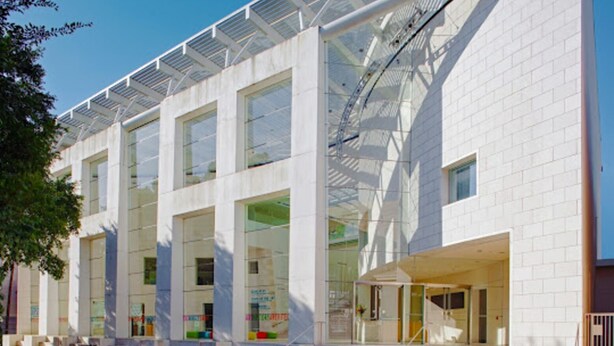Un edificio moderno con ampie vetrate, un ingresso coperto e una struttura metallica sul tetto.