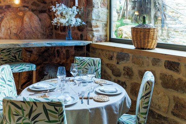 A dining area with a stone wall, a window with a view, and a table set with plates, glasses, and cutlery.