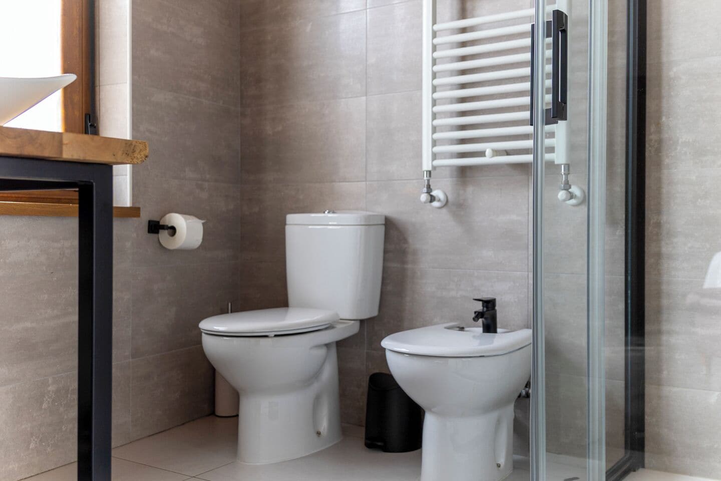 Een moderne badkamer met twee toiletten, een glazen douchecabine en een handdoekrek.