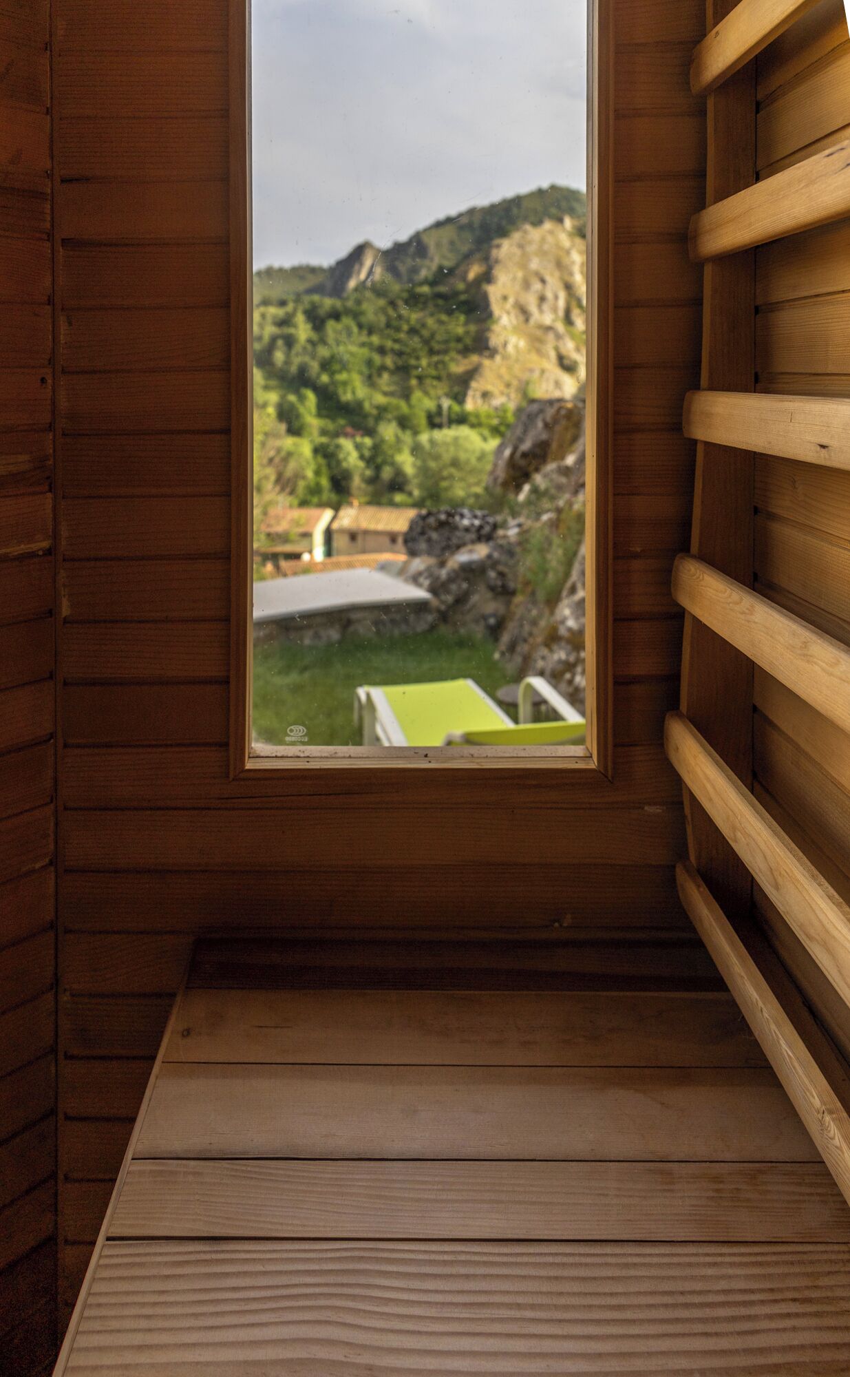 Una cabaña de madera con una ventana que da a un paisaje verde y un edificio.