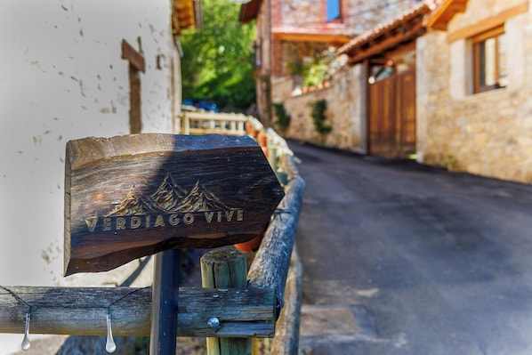 Un letrero de madera con un diseño de montaña y el texto 'VERDIGO VIVE' en una calle rústica.