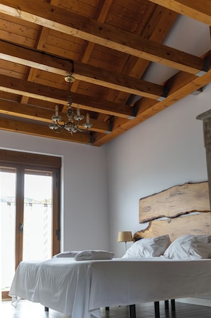 A bedroom with a wooden ceiling, a bed with white linens, a wooden headboard, and a window with a view.