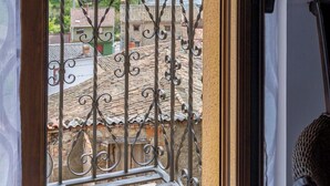 Ein Balkon mit schmiedeeisernen Geländern mit Blick auf eine gebirgige Landschaft und Gebäude mit Terrakotta-Dächern.