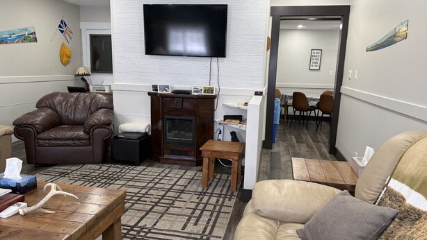 A living room with a leather sofa, a television, a fireplace, and a dining area with chairs. - The Trailway Hub, ideally located in Deer Lake, 10 minutes from the airport (Deer Lake)
