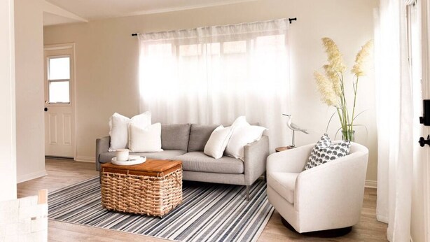 Una sala de estar con un sofá gris, un sillón blanco, una mesa de centro de madera y un tapete a rayas.