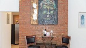 Ein Essbereich mit Backsteinwand, zwei Holzsesseln, einem Glastisch und einem Buddha-Gemälde.