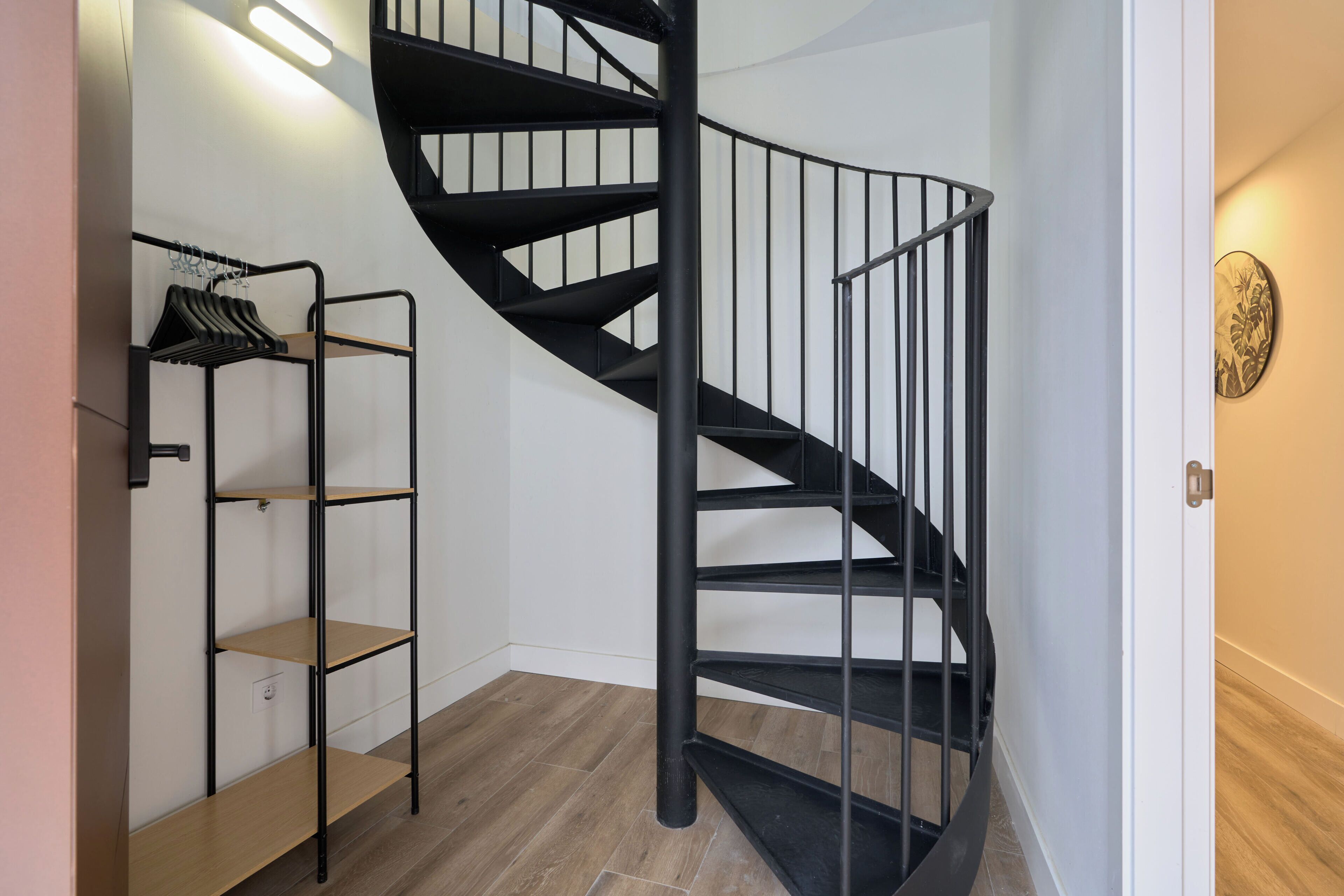 A modern interior with a spiral staircase, wooden flooring, and a metal shelving unit with clothes.
