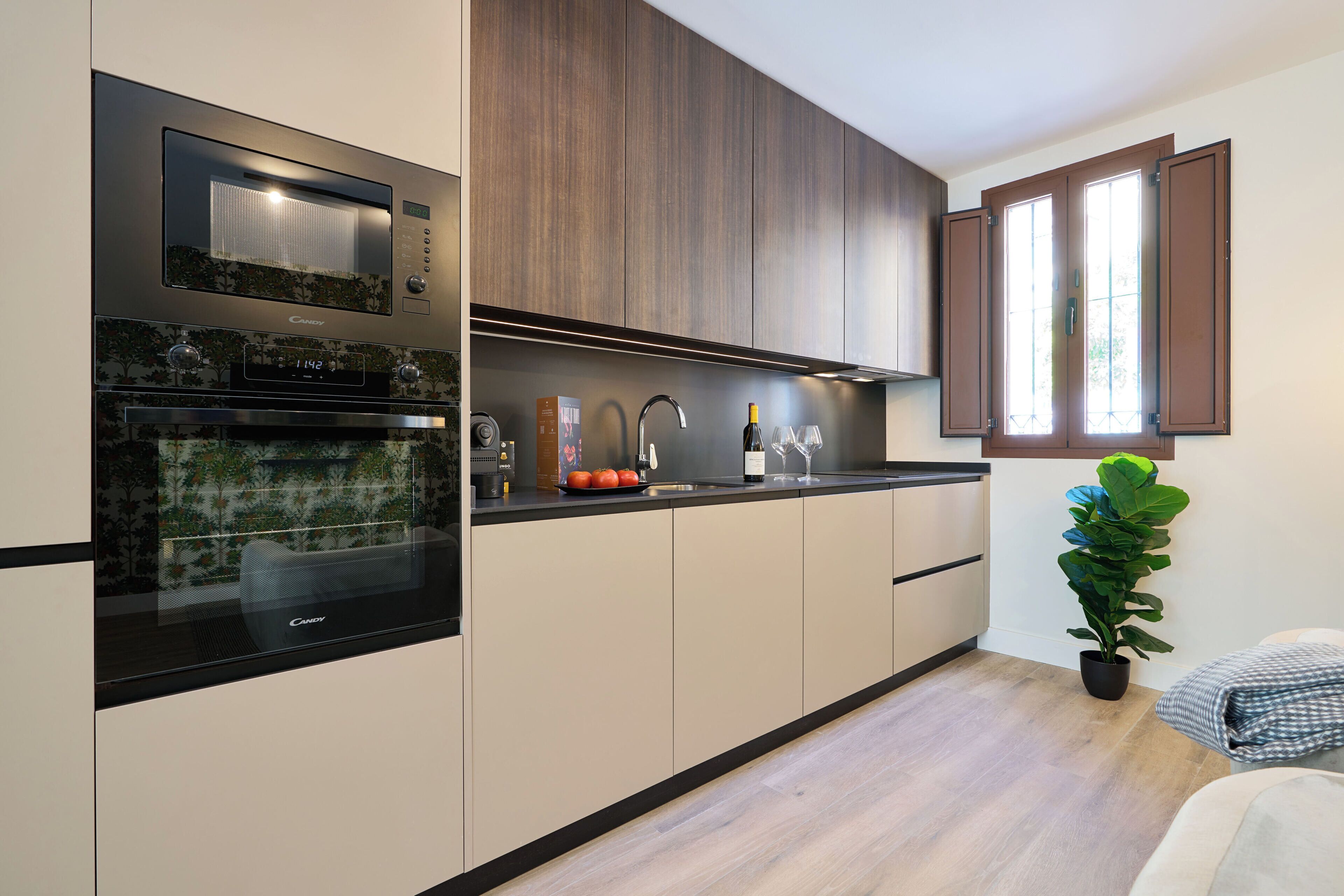 A modern kitchen with built-in appliances, a sink, and a window with wooden shutters.