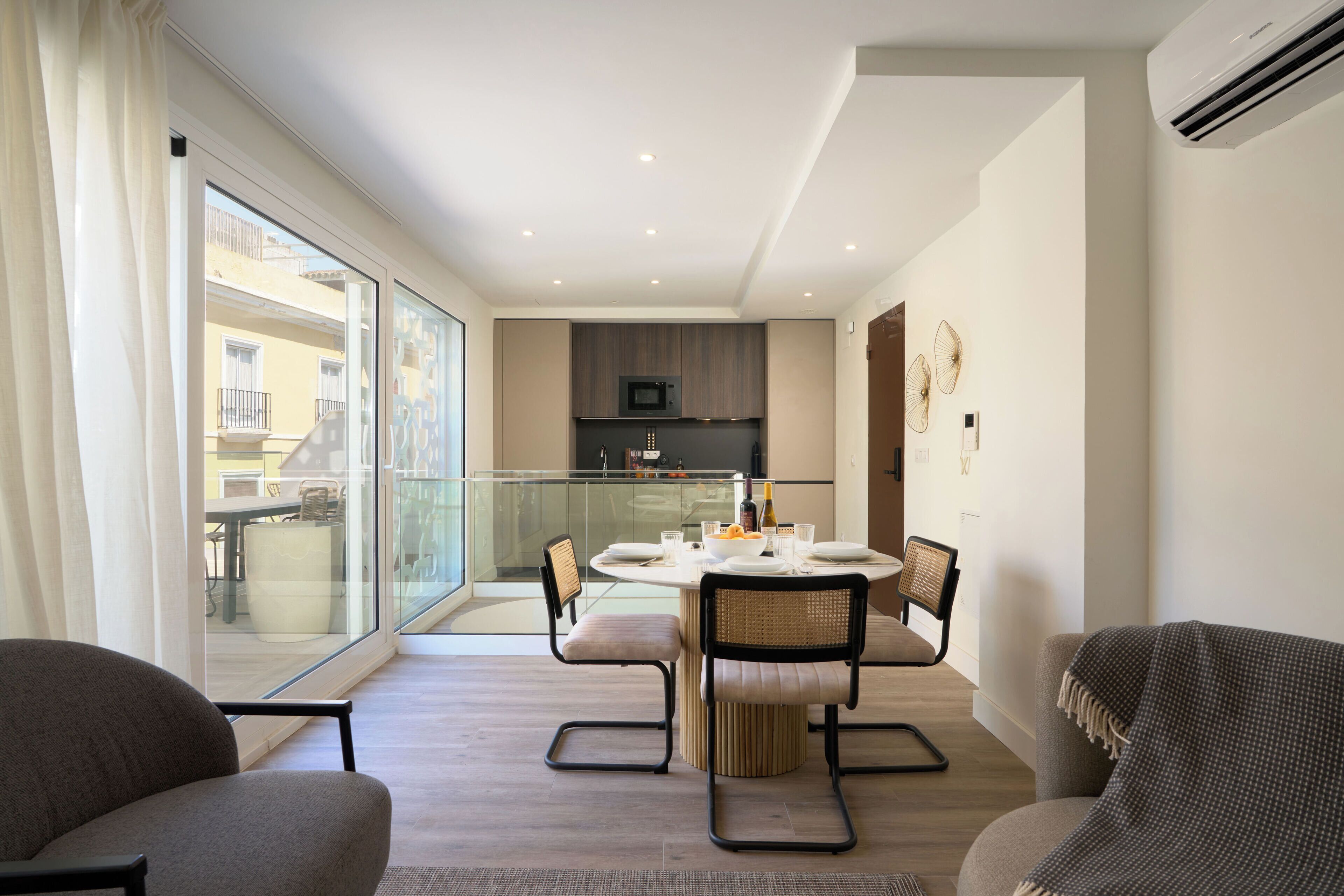 Una sala de estar moderna con comedor, ventanas amplias y una cocina al fondo.
