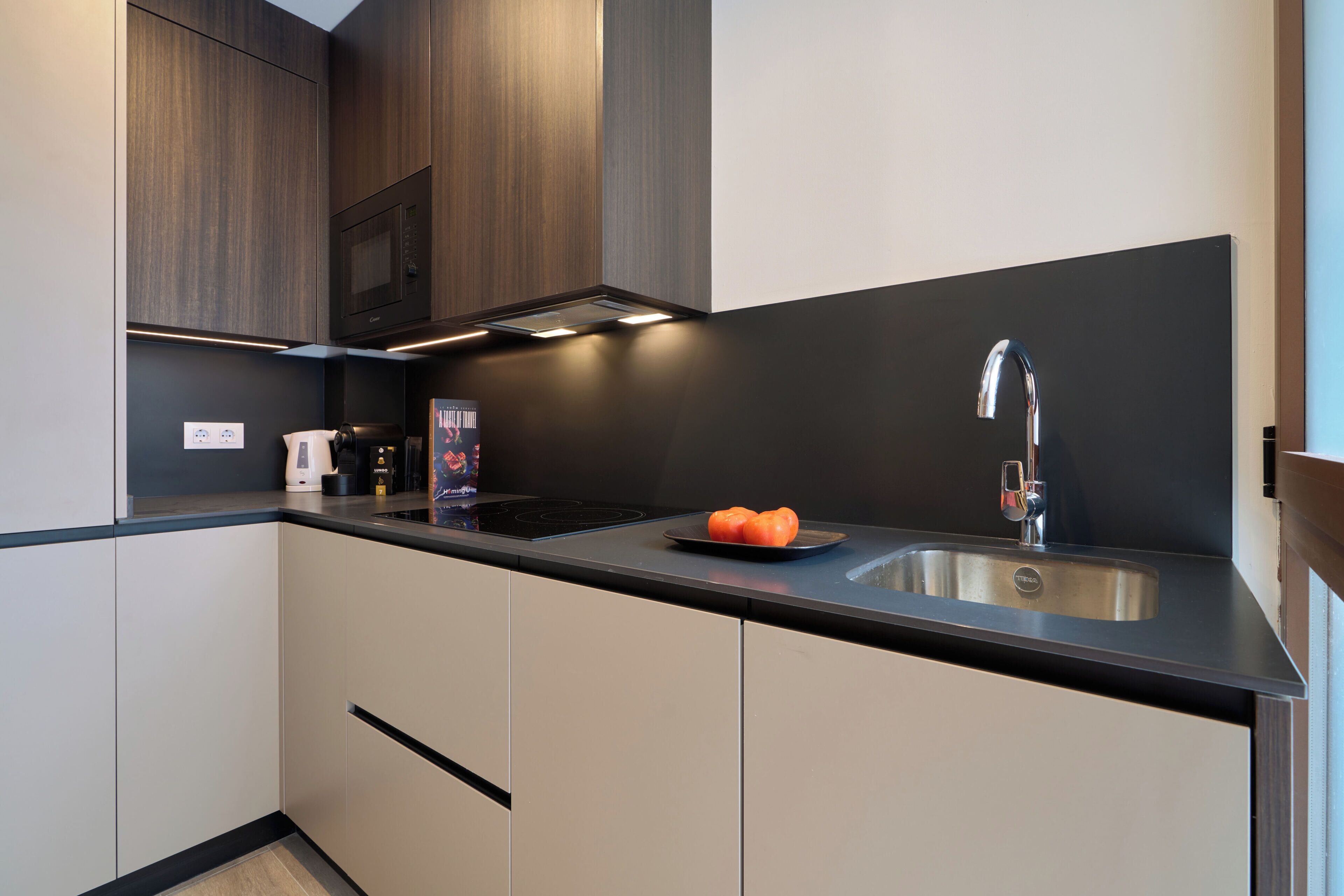 A modern kitchen with dark wood cabinets, a black countertop, a stainless steel sink, and a built-in microwave.