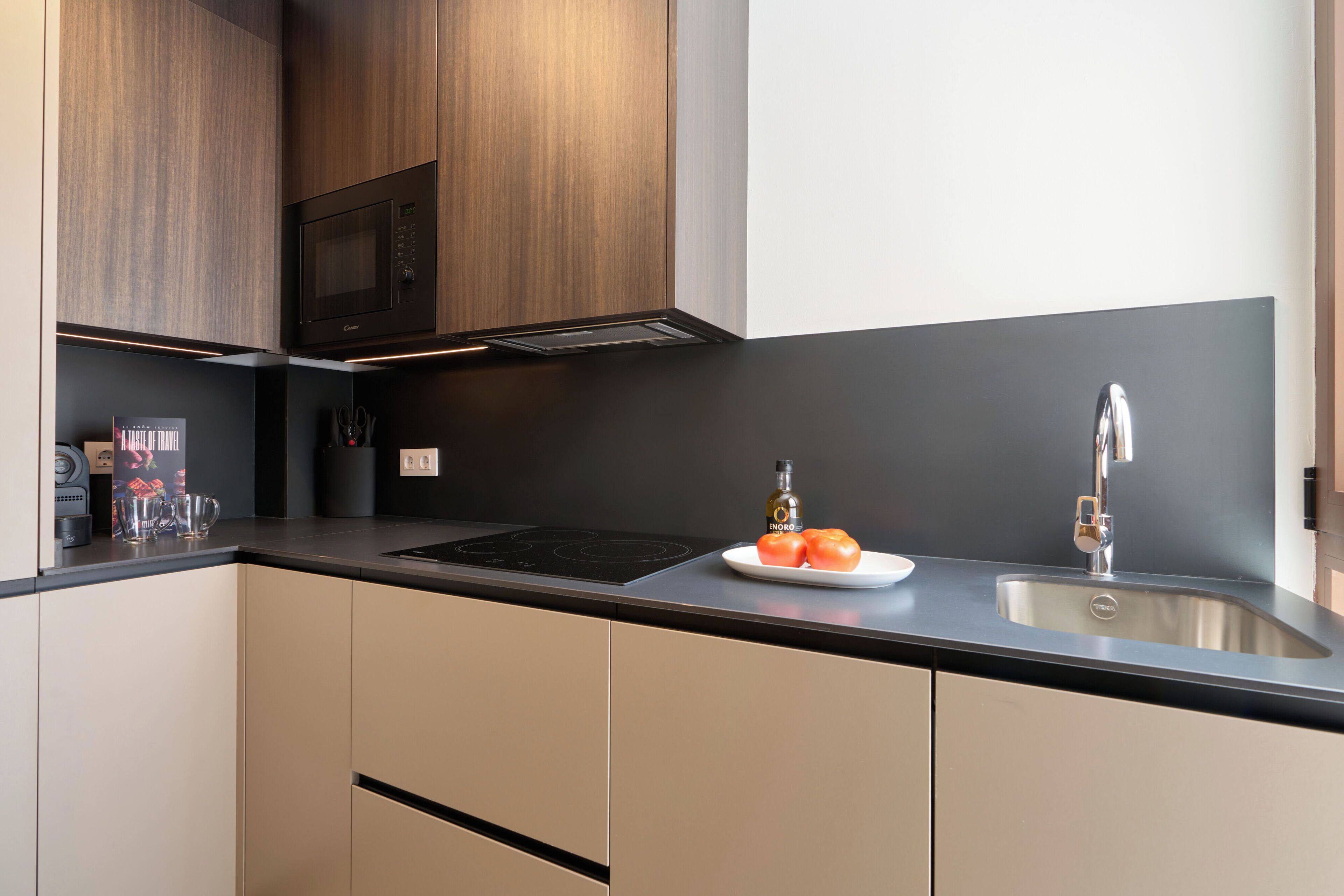 A modern kitchen with a built-in microwave, a sink, and a countertop with a plate of tomatoes.