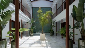 A spacious indoor area with a tiled floor, potted plants, and a central column. - Casa Pizarro, by Homing U (Seville)