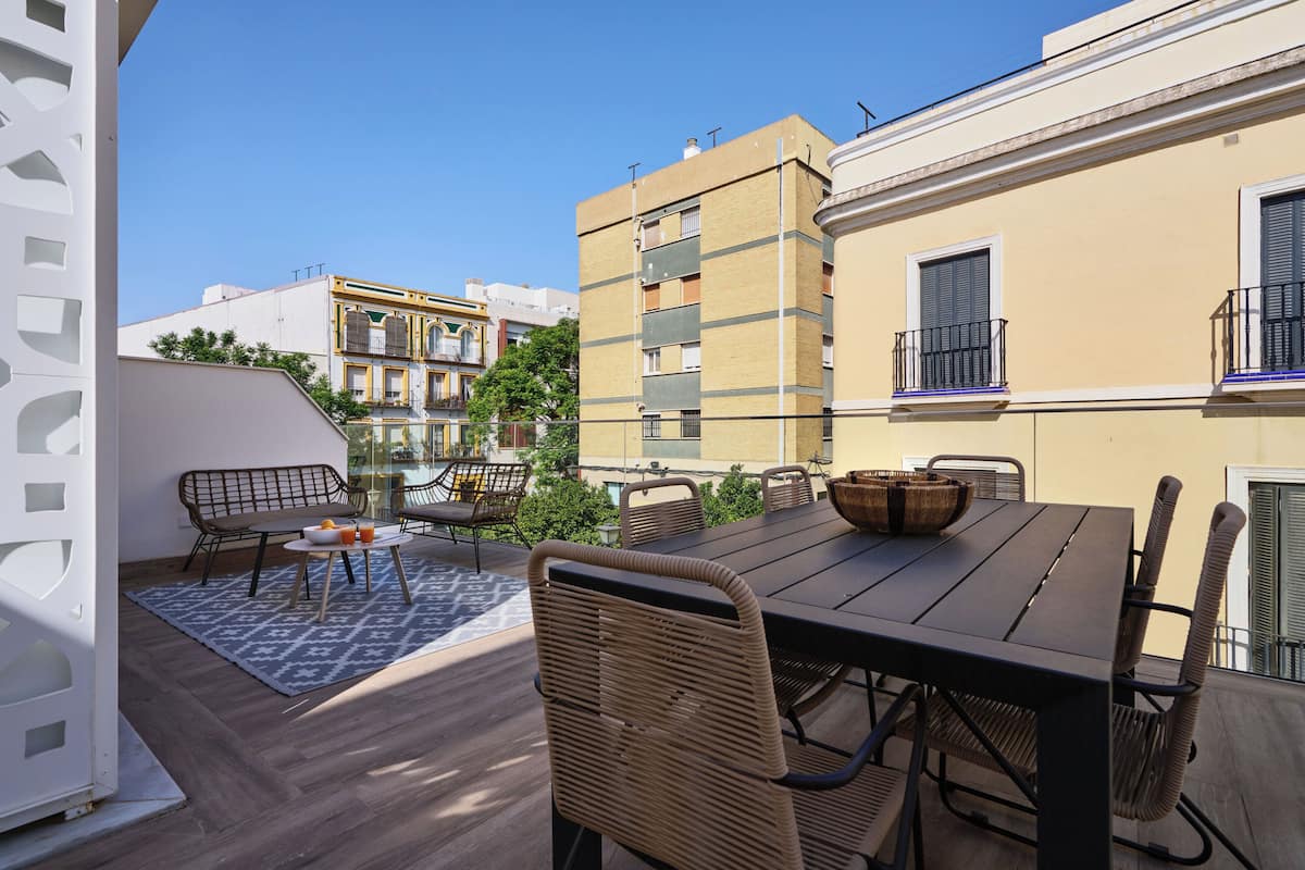 Une terrasse extérieure avec une table en bois et des chaises en osier, entourée d’une clôture blanche décorative.