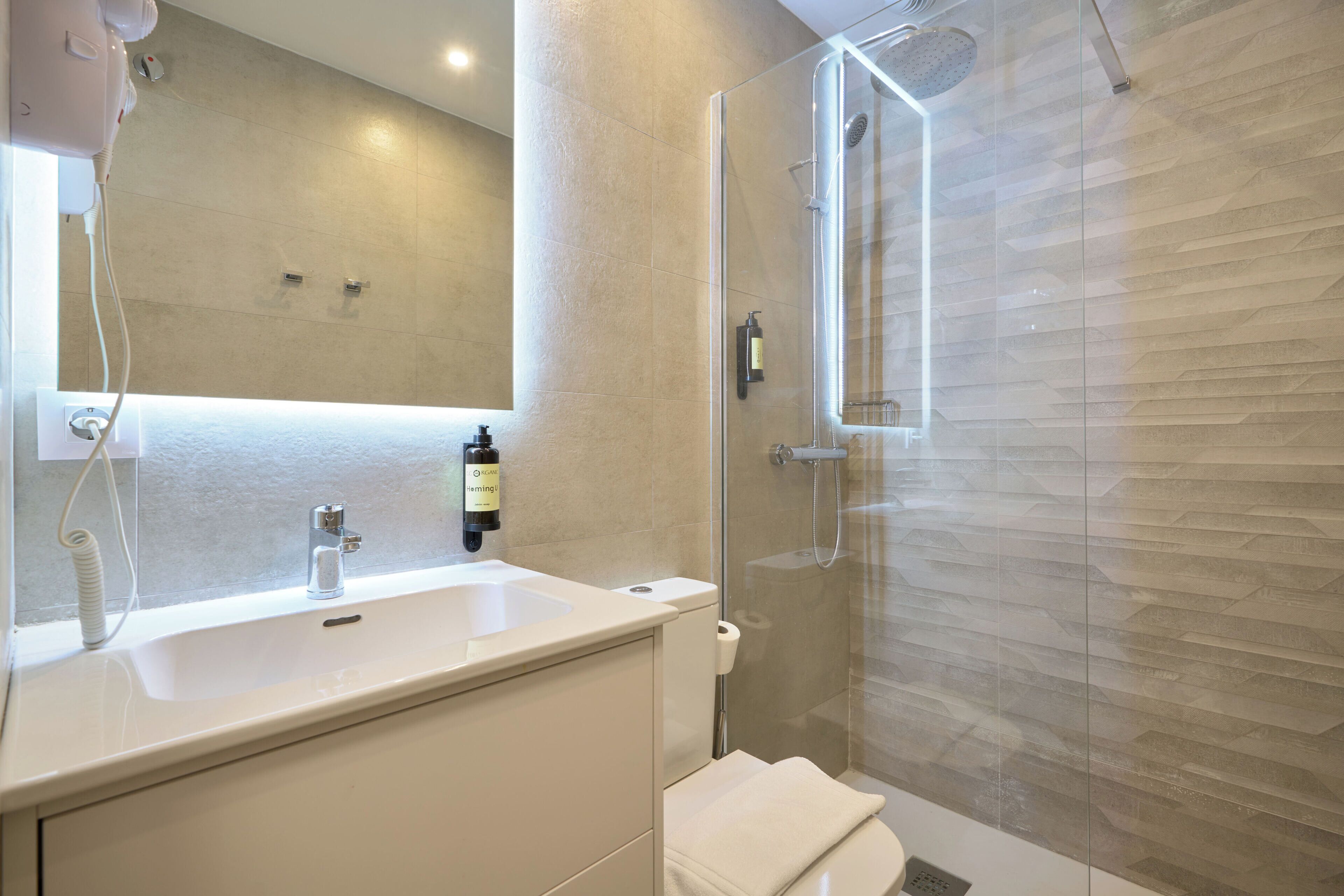 Un baño moderno con cabina de ducha de vidrio, un espejo grande y un lavabo blanco.