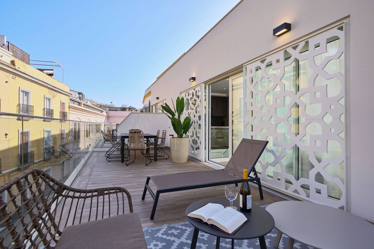 Un balcon avec une table, des chaises, un pot de fleurs et une bouteille de vin.