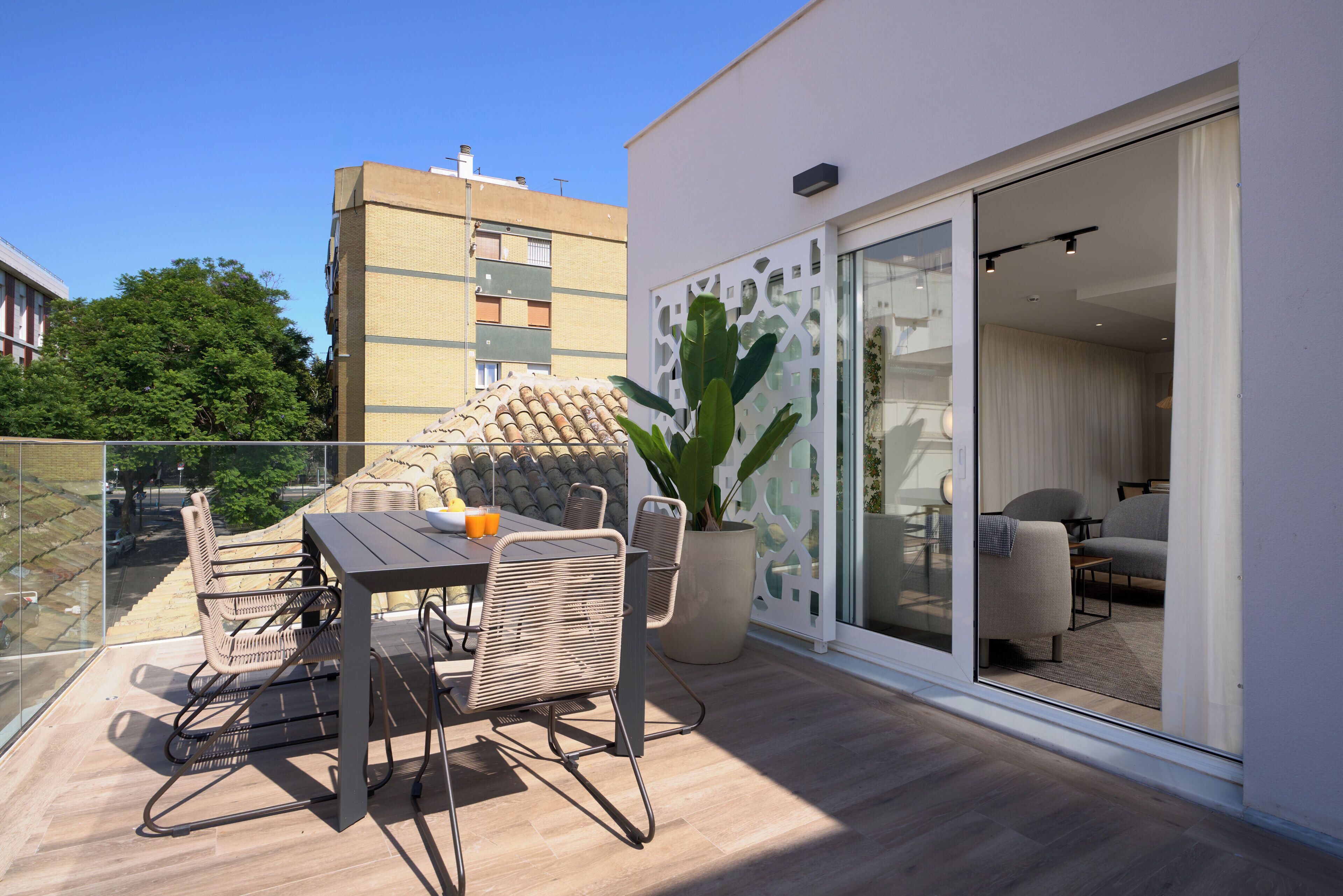 A balcony with a table and chairs, a potted plant, and a view of a building in the background.